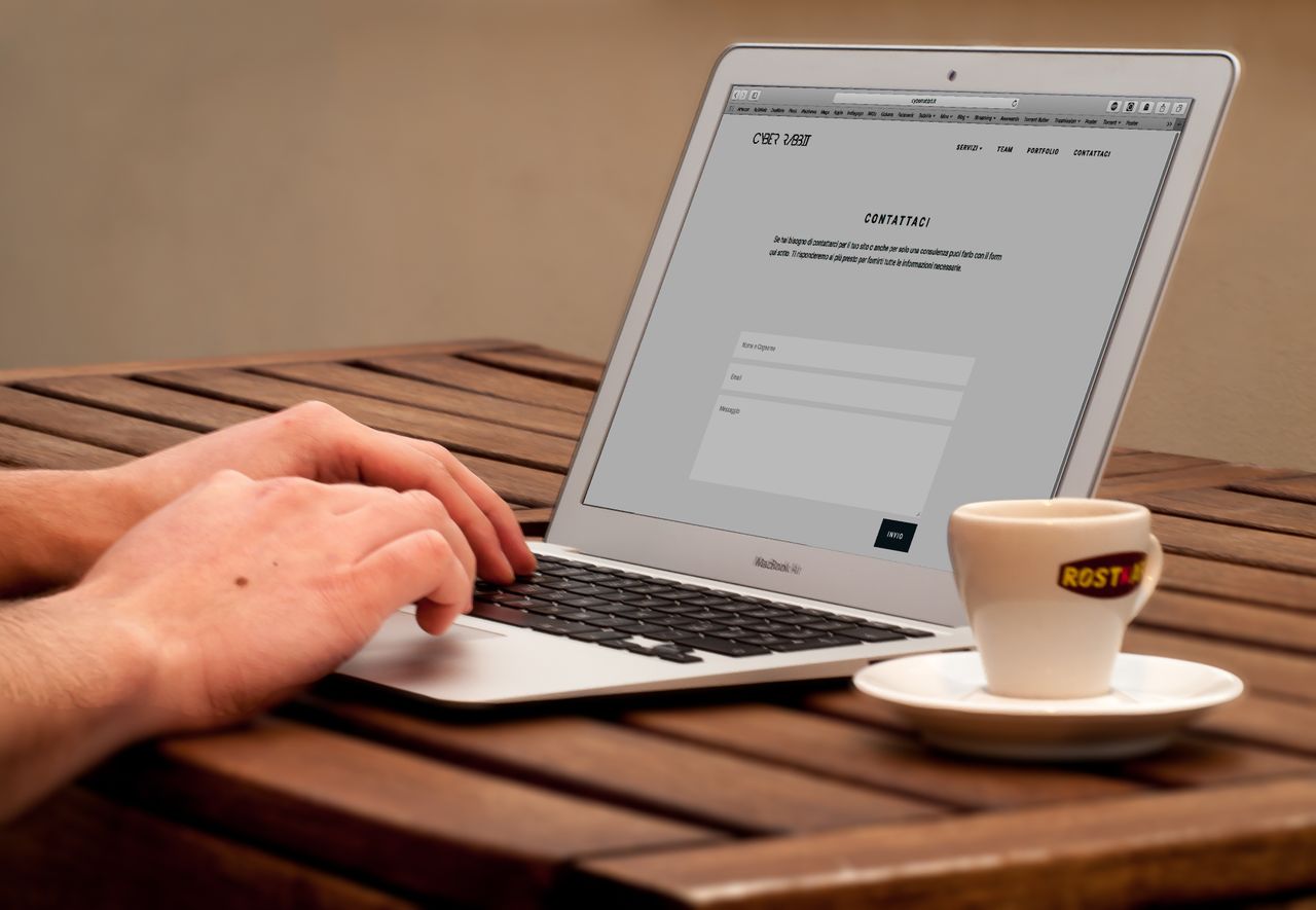 Mastering the First Impression: Your intriguing post title goes here Close-up of hands typing on a laptop next to a cup of coffee on a wooden desk.