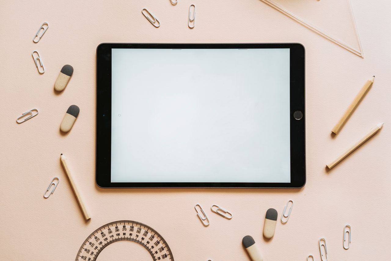 Services A tablet surrounded by stationery items like pencils, erasers, and paper clips in a flat lay setup.