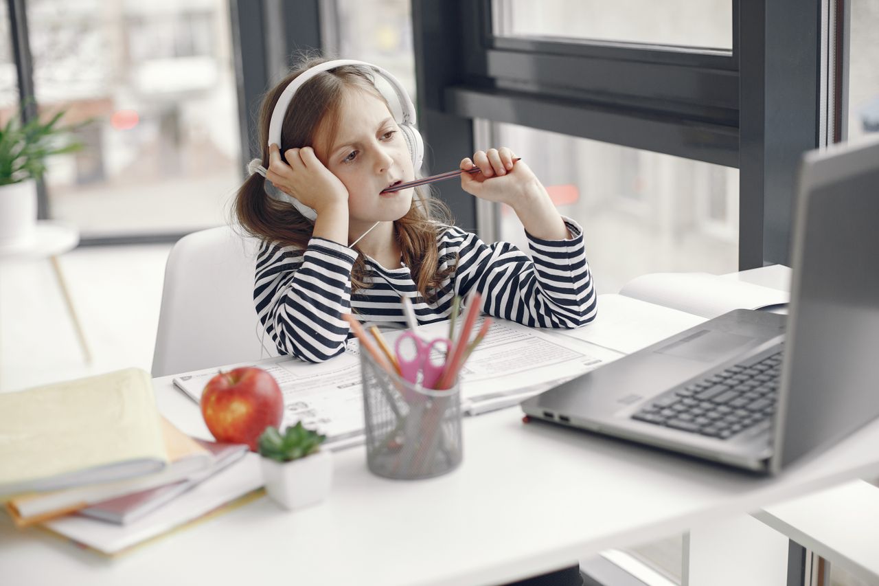 Services A child wearing headphones doing homework on a laptop indoors. Remote learning setup.